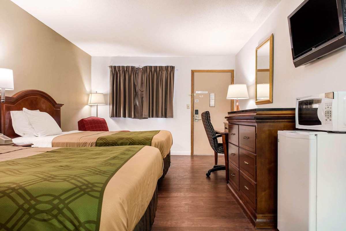 A hotel room with two beds, a desk with a chair, a television, a microwave, and a refrigerator.