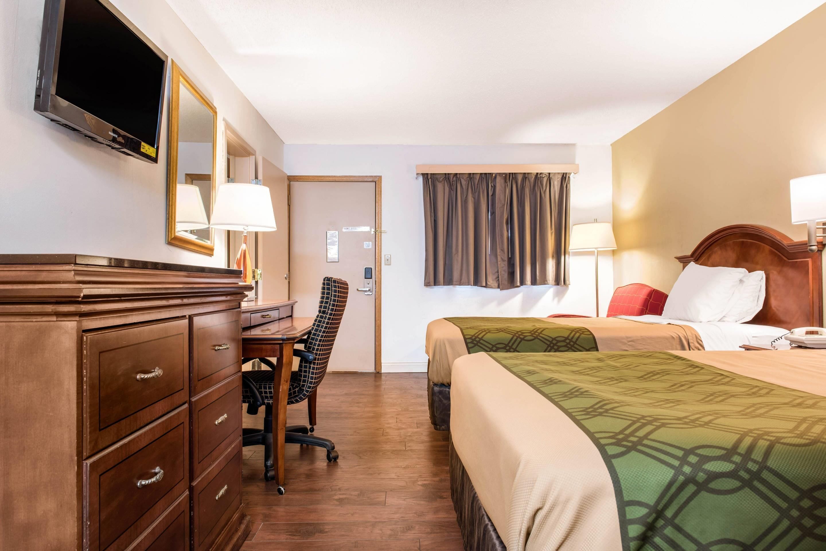 Een hotelkamer met een bureau, stoel, twee bedden, een televisie en een spiegel.