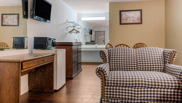A room with a wooden desk, a television, a kitchenette, a patterned sofa, and a mirror.