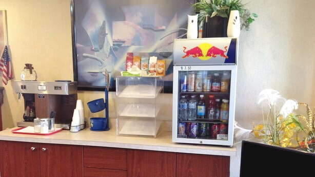 Zona de recepción con máquina de café, dispensador de bebidas y televisor.