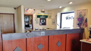 Una zona de recepción con mostrador de madera, carteles que indican Desayuno Continental y Bienvenida a America’s Best Inn, y un letrero de VERO.