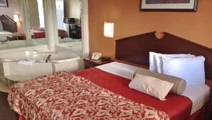 Habitación de hotel con una cama grande, baño privado con bañera, espejo y escritorio con teléfono.