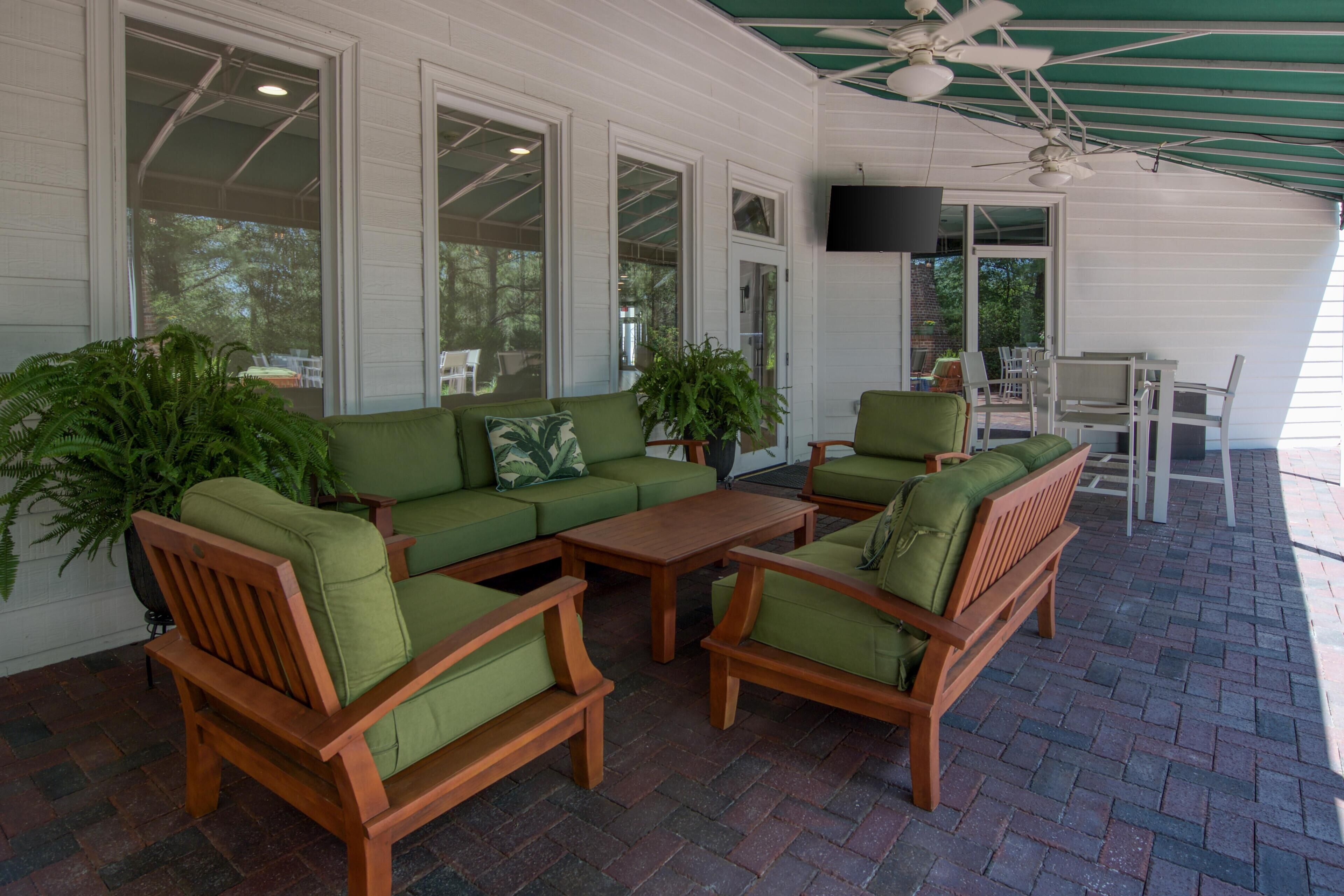 A covered patio area with wooden furniture, large windows, and a ceiling fan.