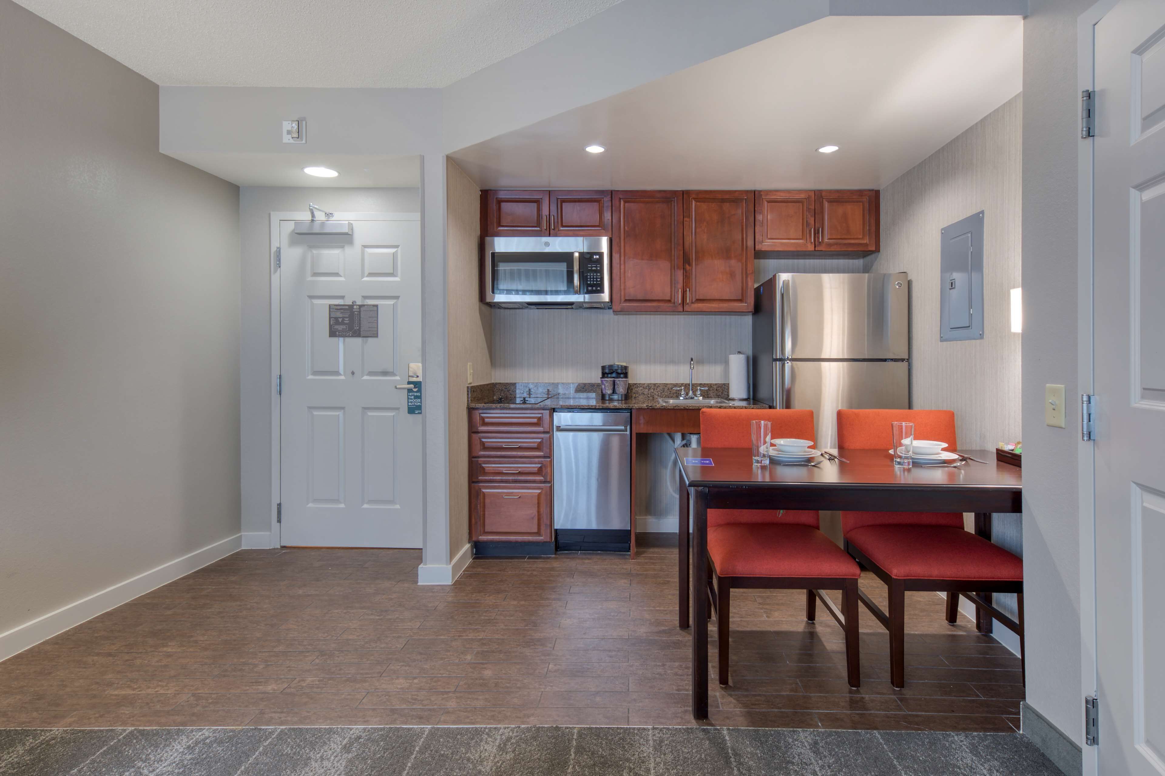 A compact kitchen with wooden cabinets, stainless steel appliances, and a dining area with red chairs.