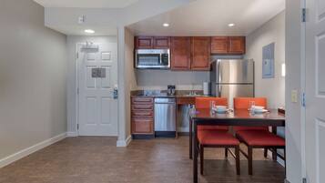 A compact kitchen with wooden cabinets, stainless steel appliances, and a dining area with red chairs.