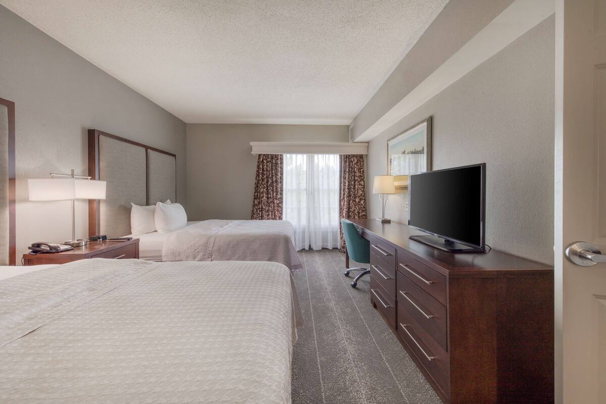 A hotel room with two beds, a desk with a television, a chair, and a dresser.