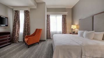 A hotel room with a large bed, a television, an orange chair, and patterned curtains.