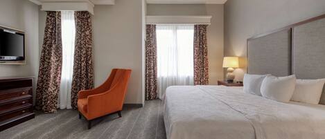 A hotel room with a large bed, a television, an orange chair, and patterned curtains.