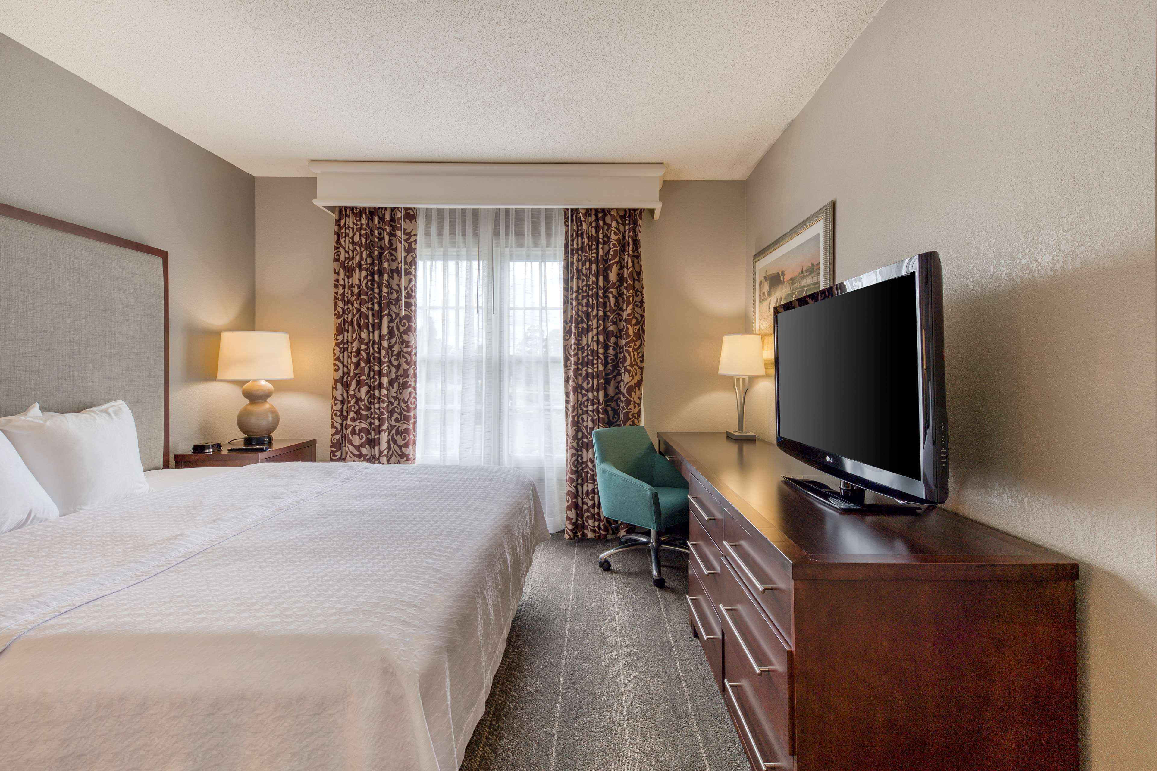 A hotel room with a bed, a desk with a television, a chair, and two lamps.