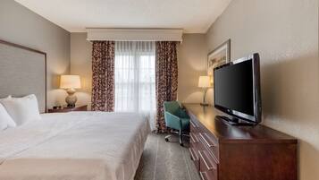 A hotel room with a bed, a desk with a television, a chair, and two lamps.