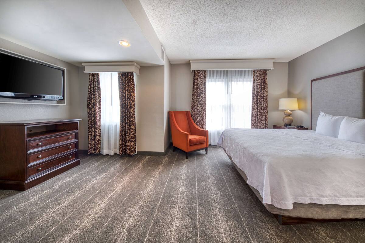 A hotel room with a bed, a TV, a dresser, and a chair.