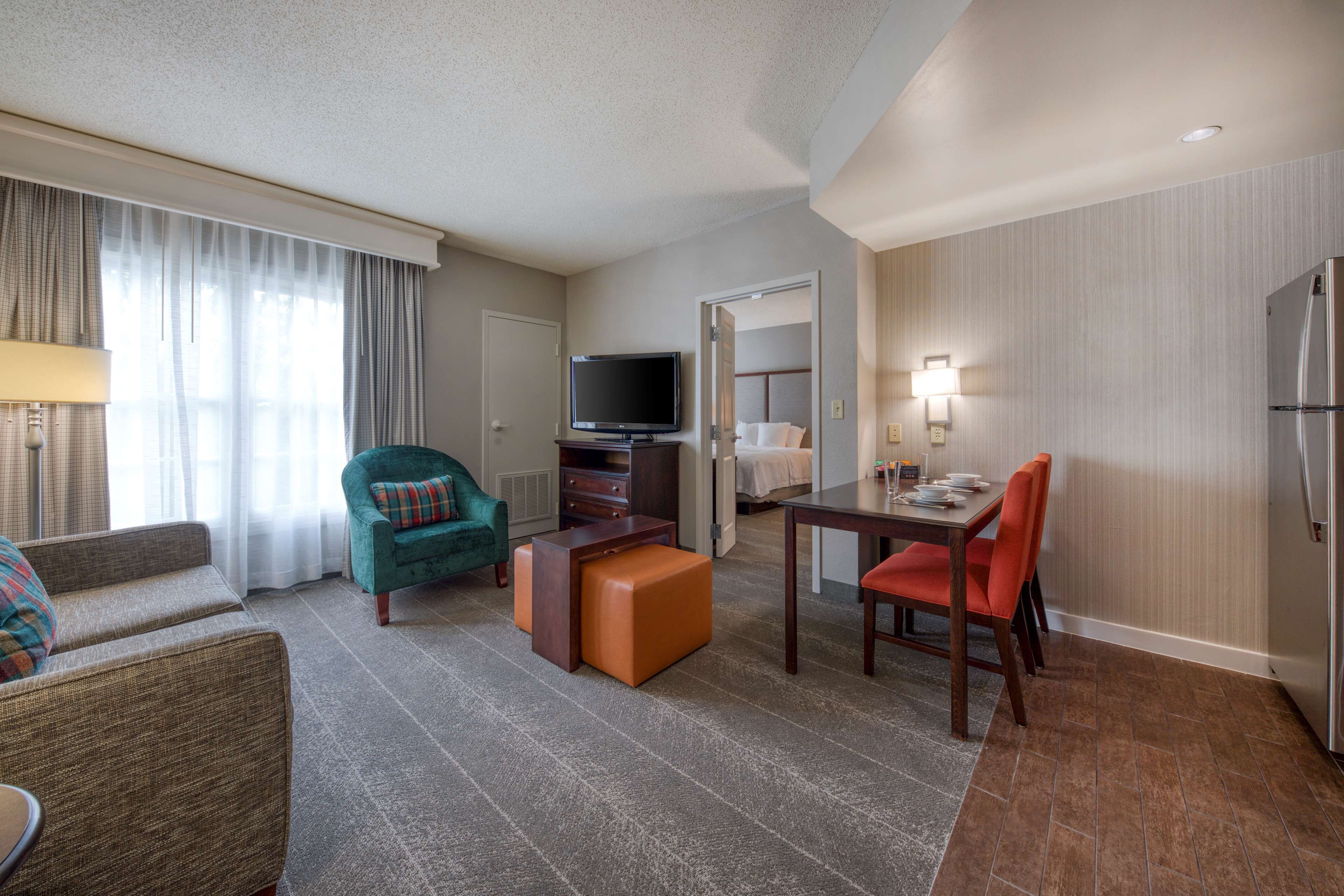 A hotel room with a living area, a dining table, a television, and a kitchenette.
