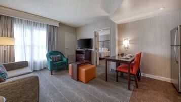 A hotel room with a living area, a dining table, a television, and a kitchenette.
