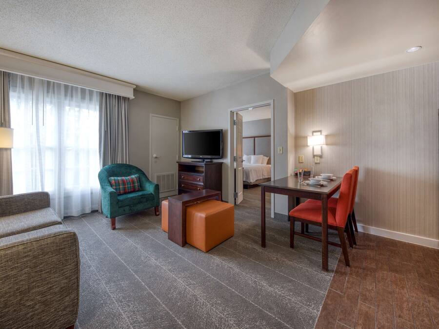 A hotel room with a living area, a dining table, a television, and a kitchenette.