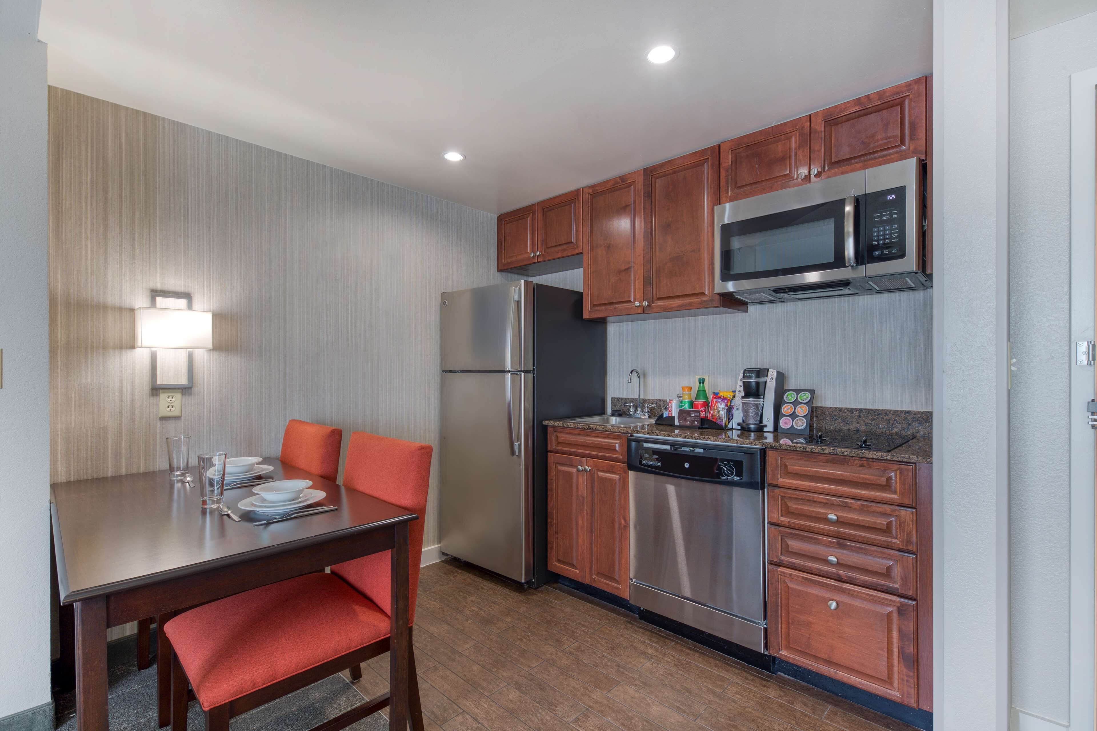 A compact kitchen with wooden cabinets, stainless steel appliances, and a dining area with a table and chairs.