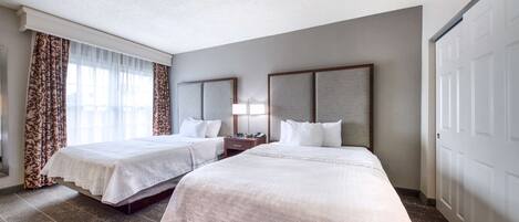 A hotel room with two beds, a nightstand, a lamp, and a large window with curtains.
