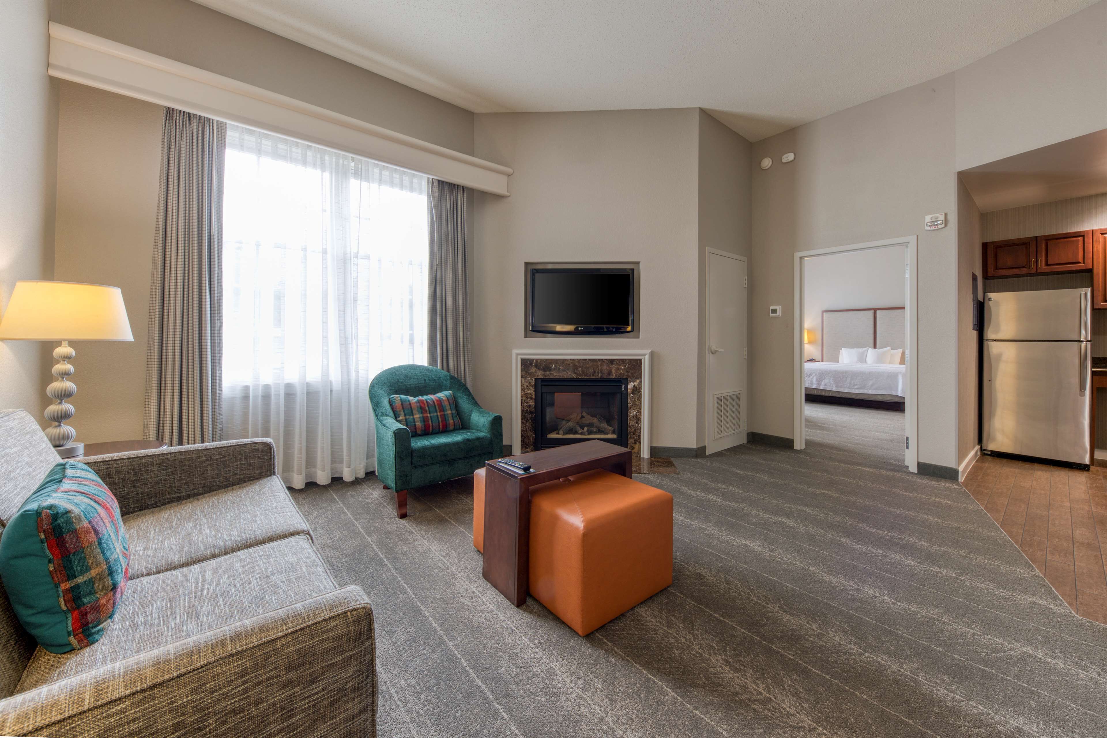 A hotel room with a sofa, armchair, ottoman, fireplace, TV, and a kitchenette.