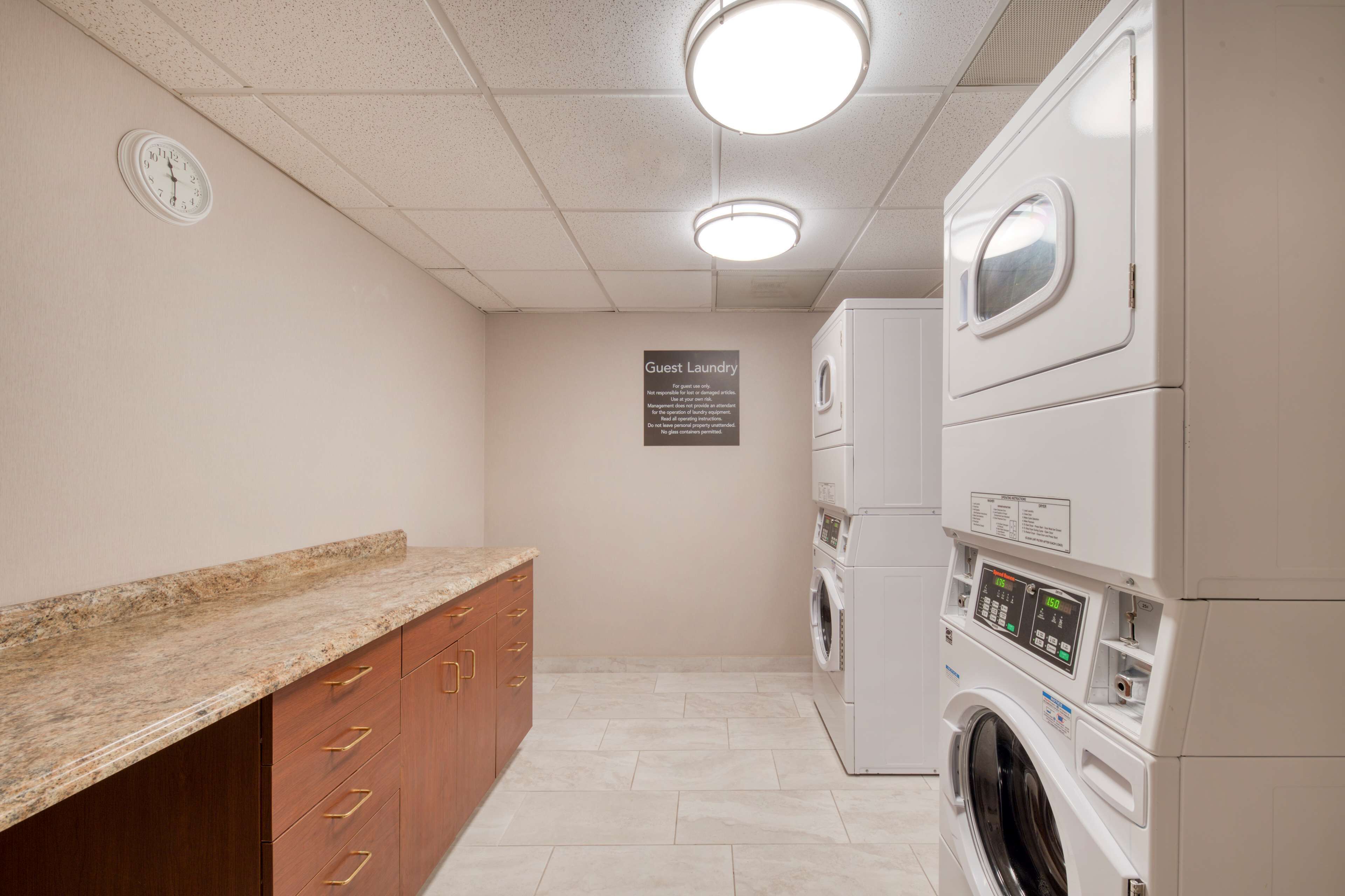 A laundry room with a granite countertop, wooden cabinets, and stacked washing machines.