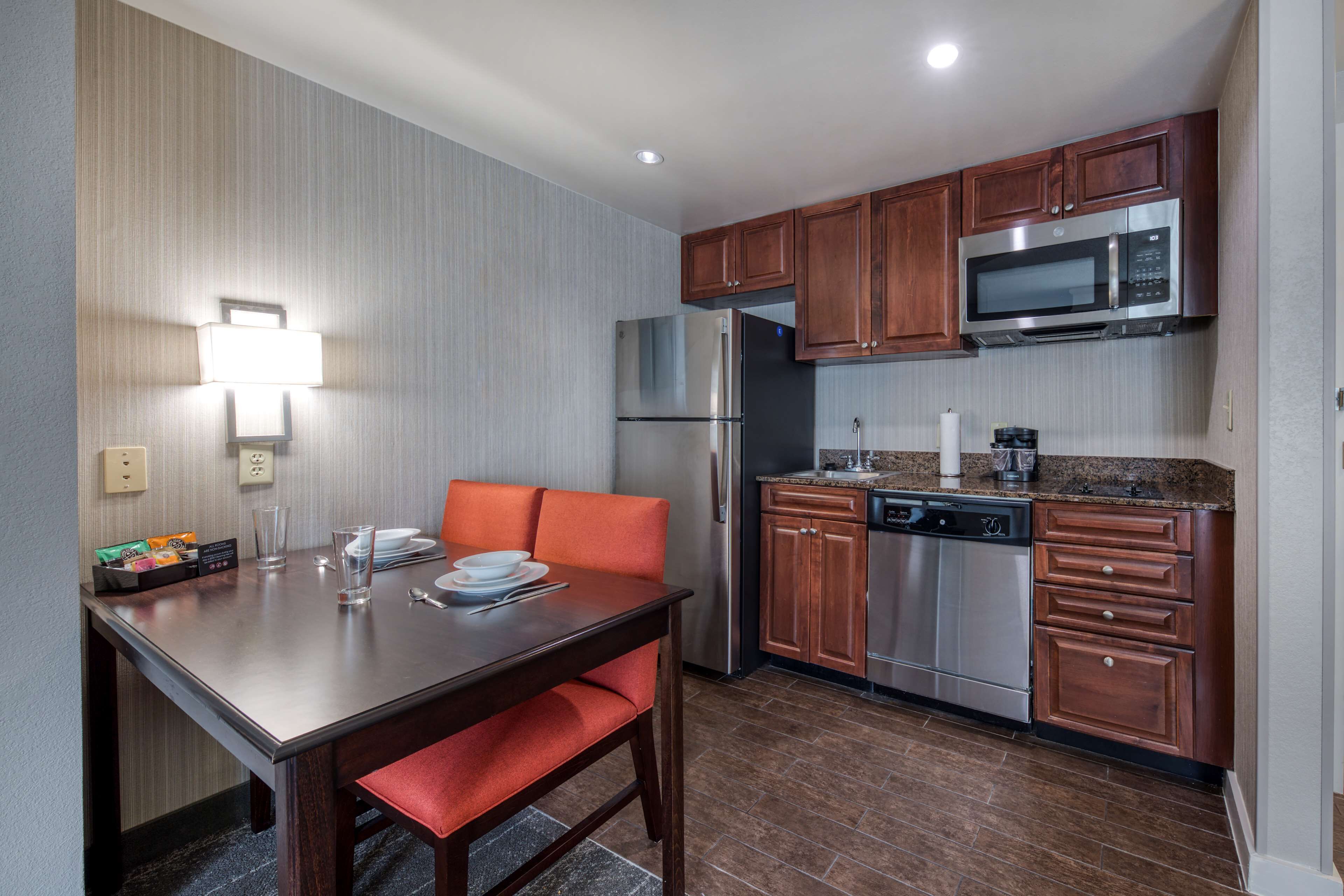 A compact kitchen with a refrigerator, microwave, and dishwasher. There is a dining table with chairs and a small countertop with a coffee maker.