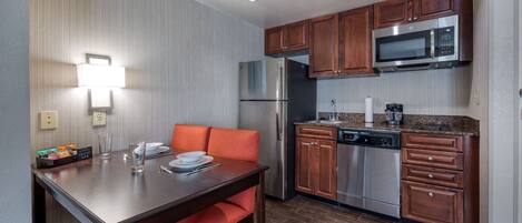A compact kitchen with a refrigerator, microwave, and dishwasher. There is a dining table with chairs and a small countertop with a coffee maker.