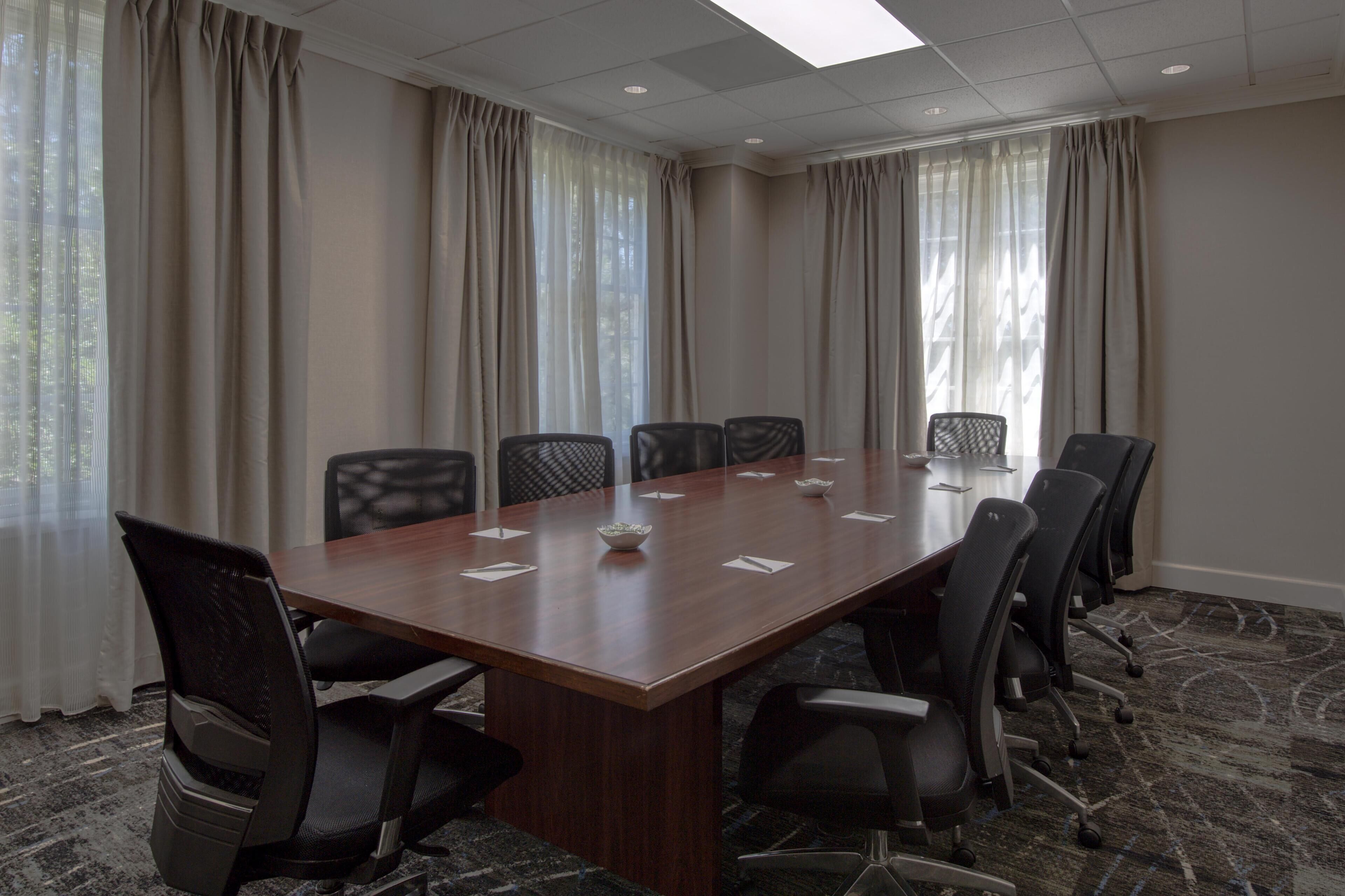 A conference room with a long table, chairs, and curtains.