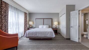 A hotel room with a bed, a nightstand, a lamp, a chair, and a bathroom door.
