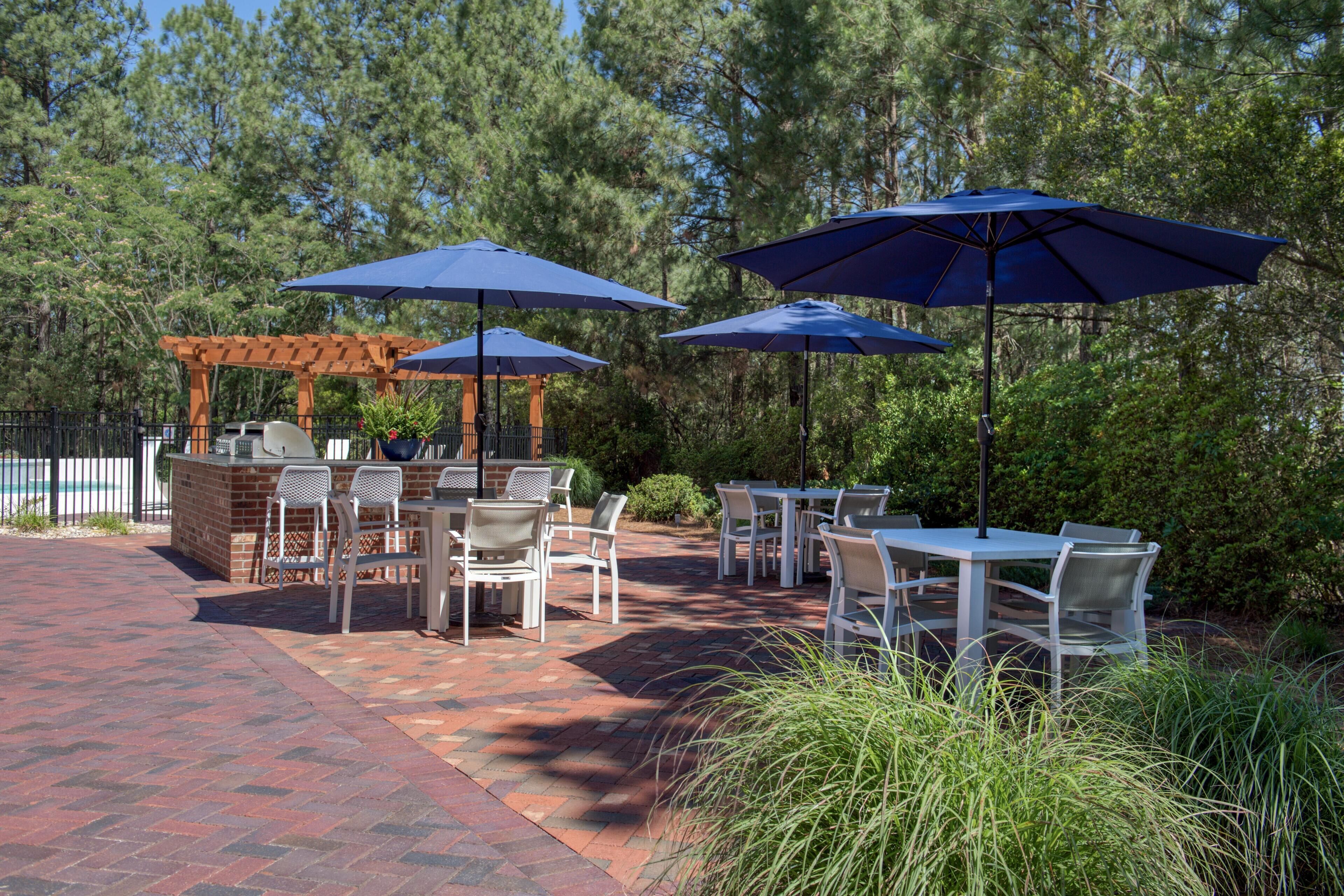 An outdoor patio with tables and chairs, blue umbrellas, and a brick pathway.