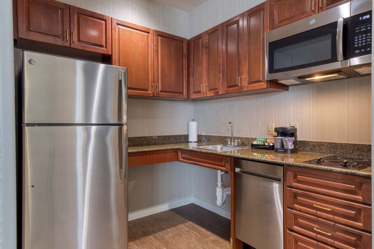A kitchen with stainless steel appliances, wooden cabinets, granite countertops, and a built-in microwave.