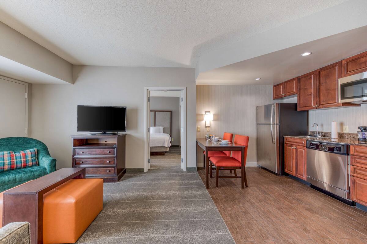 A modern hotel room with a living area, kitchenette, and a separate bedroom.