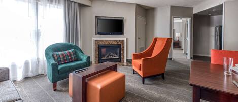 A hotel room with a fireplace, a television, a dining table, and two armchairs.