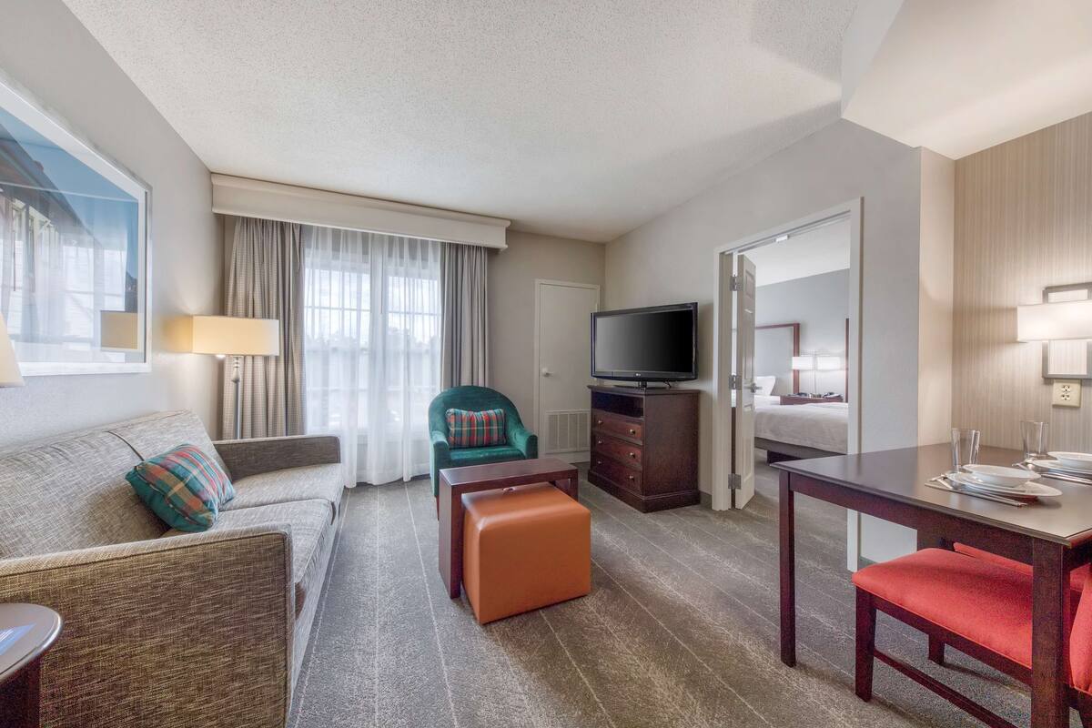 A hotel room with a sofa, armchair, ottoman, dining table, TV, and a bed.