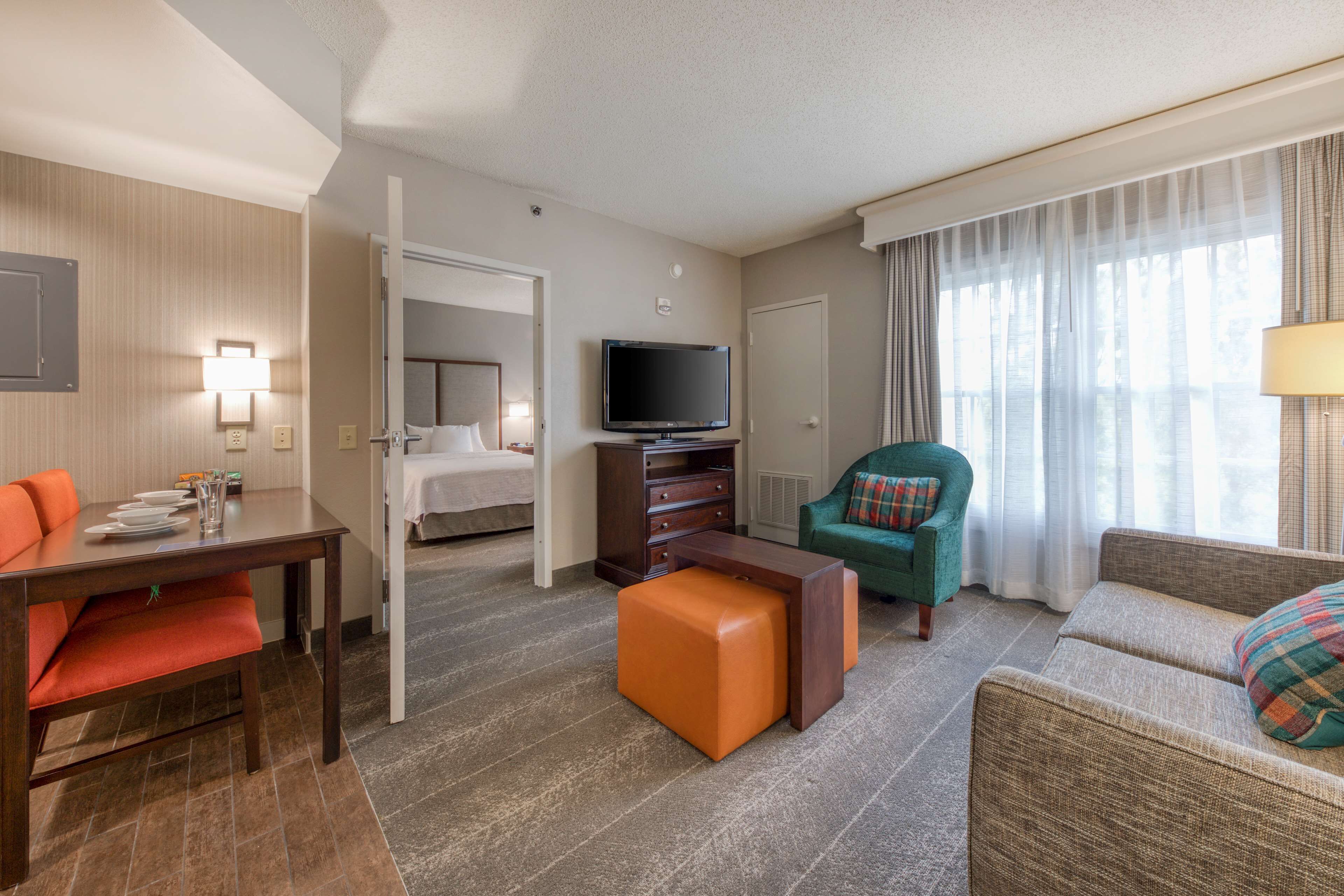 A hotel room with a dining table, a sofa, a chair, a television, and a bed.