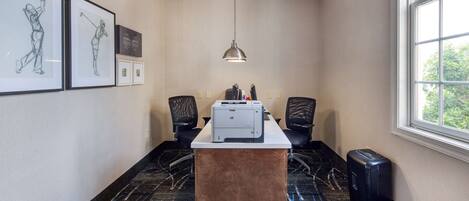 A conference room with a long table, two chairs, a printer, and framed artwork on the wall.