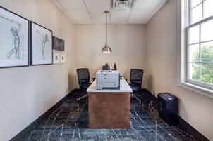 Un salón de conferencias con una larga mesa, dos sillas, una impresora y obras de arte enmarcadas en la pared.