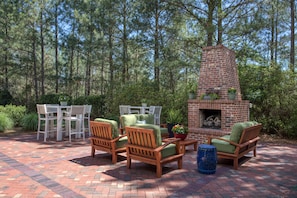 An outdoor patio with brick flooring, wooden chairs, a table, and a brick fireplace.