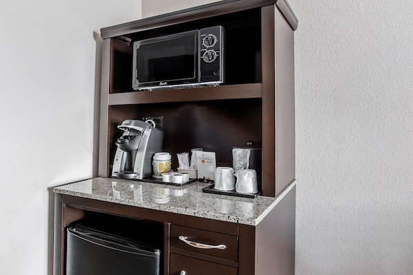 Une petite cuisine équipée d’un four à micro-ondes, d’une machine à café et d’un espace de rangement pour les capsules et les tasses de café.