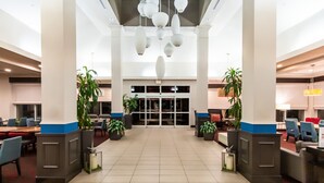 Een ruime lobby met een hoge plafond, grote ramen en moderne verlichtingsarmaturen.