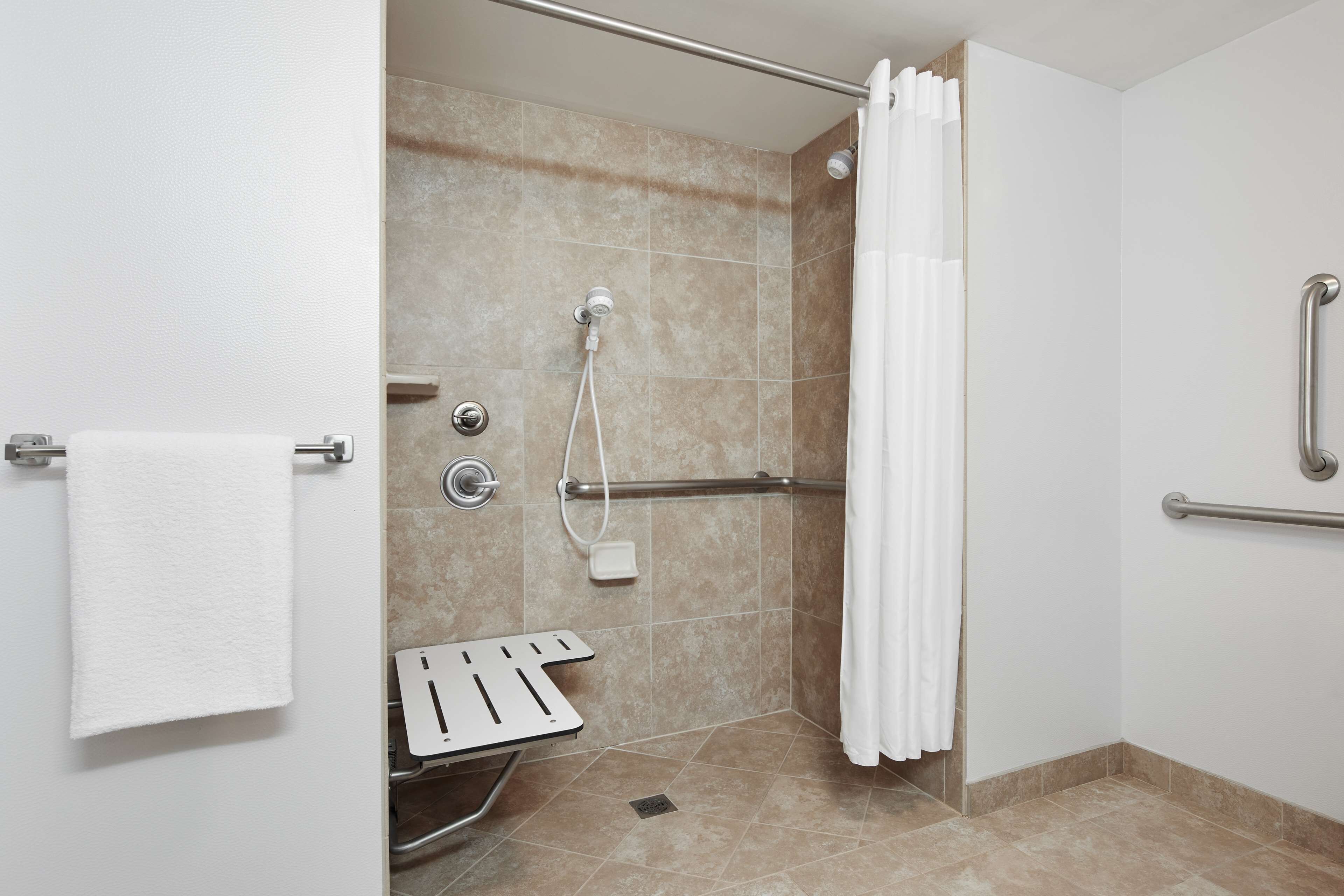 A modern bathroom with a shower, grab bars, a towel rack, and a hand dryer.