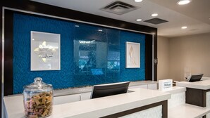 Een hotel receptie met een blauwe structuurwand, een glazen bak met snacks en een bordje met 'Hilton Honors'.