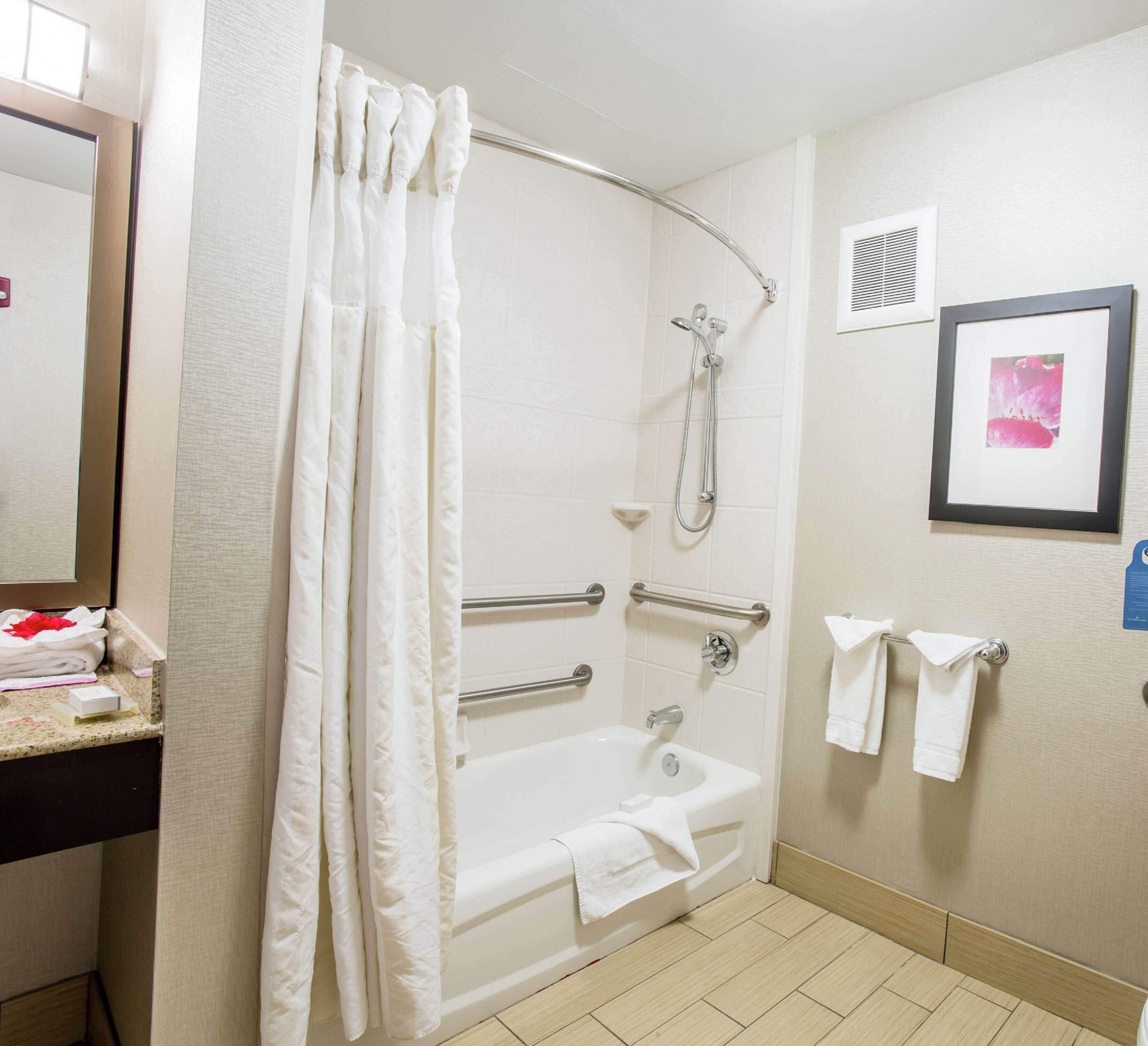 A bathroom with a bathtub, shower, and handrails.