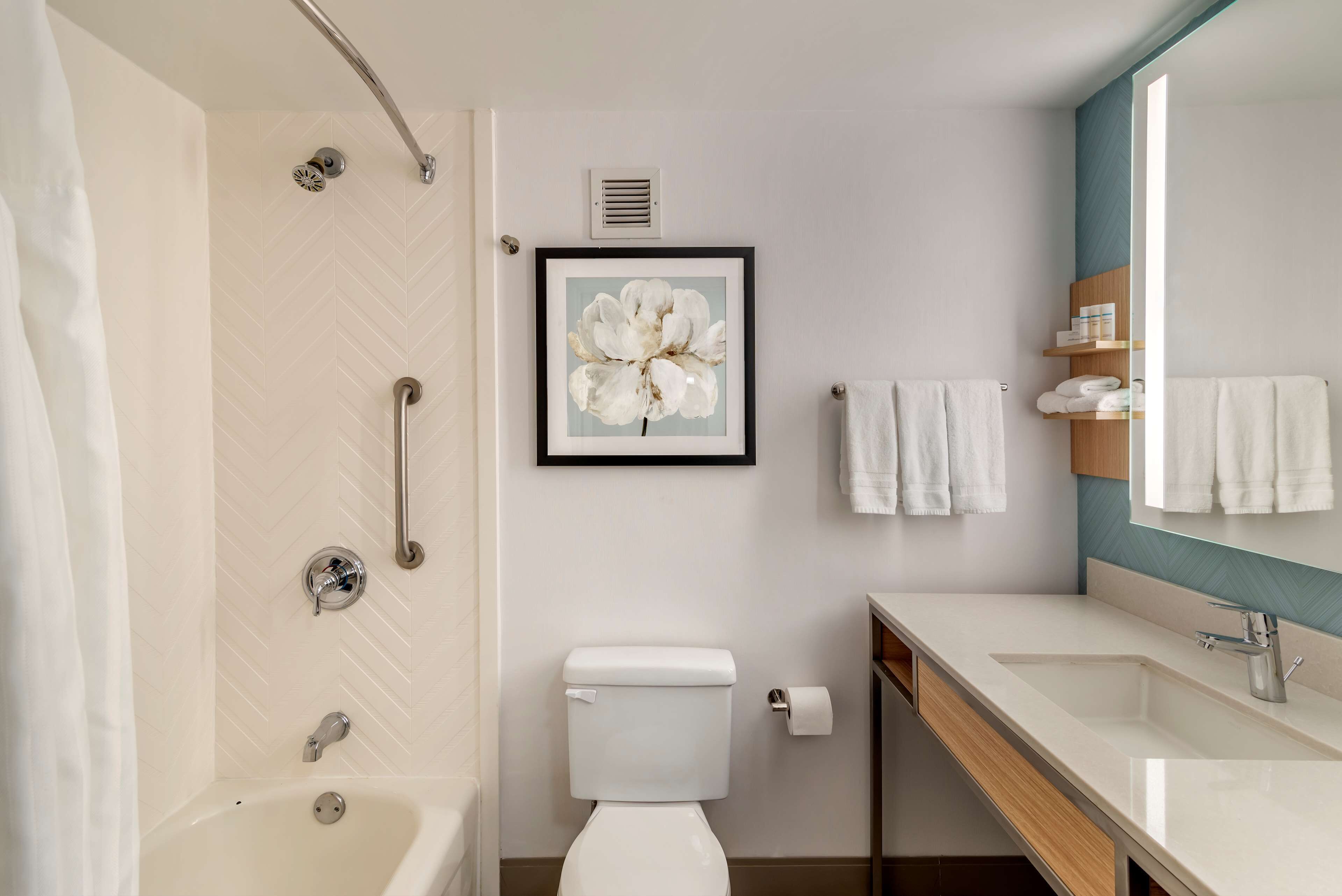 A modern bathroom with a shower, toilet, sink, and a framed floral artwork on the wall.