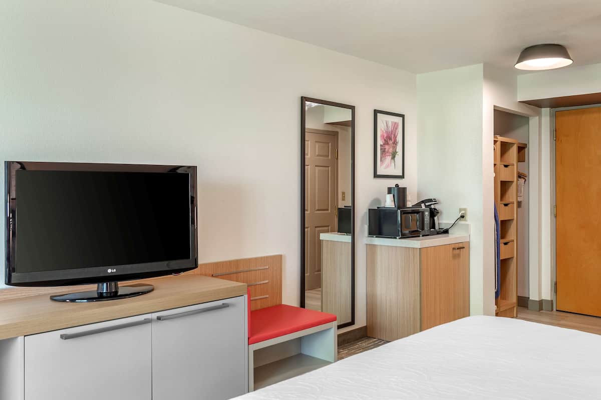 A hotel room with a bed, a TV, a desk with a chair, a mirror, and a wardrobe.