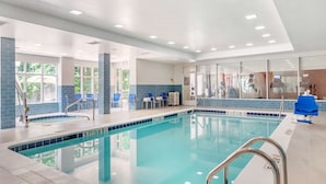 A swimming pool with clear blue water, surrounded by blue-tiled walls and a white ceiling with recessed lighting.