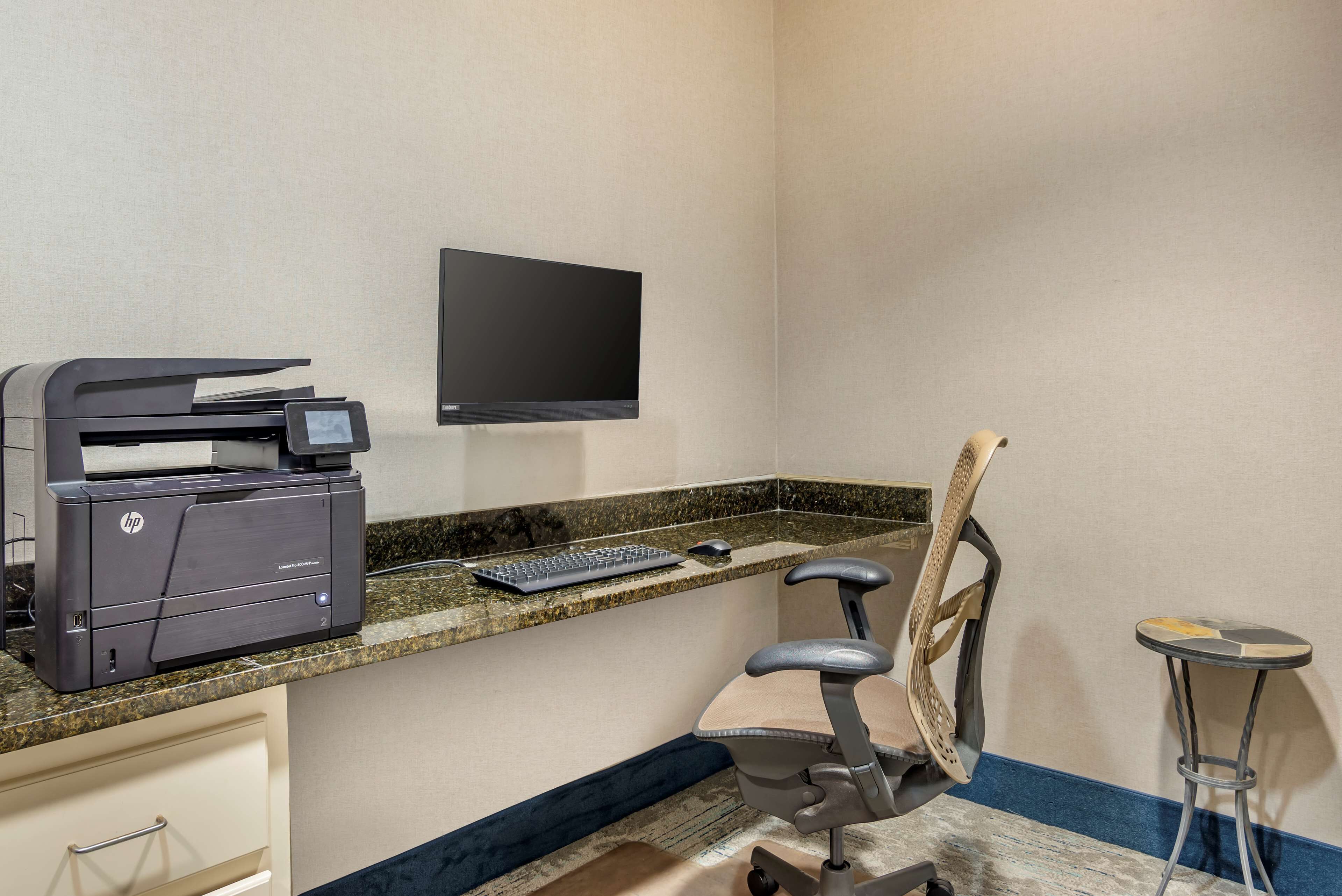Un espacio de trabajo en casa con una impresora HP, un monitor, un teclado y una silla.