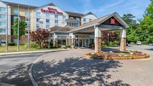 A Hilton Garden Inn with a covered entrance, a brick driveway, and a landscaped area with flowers.
