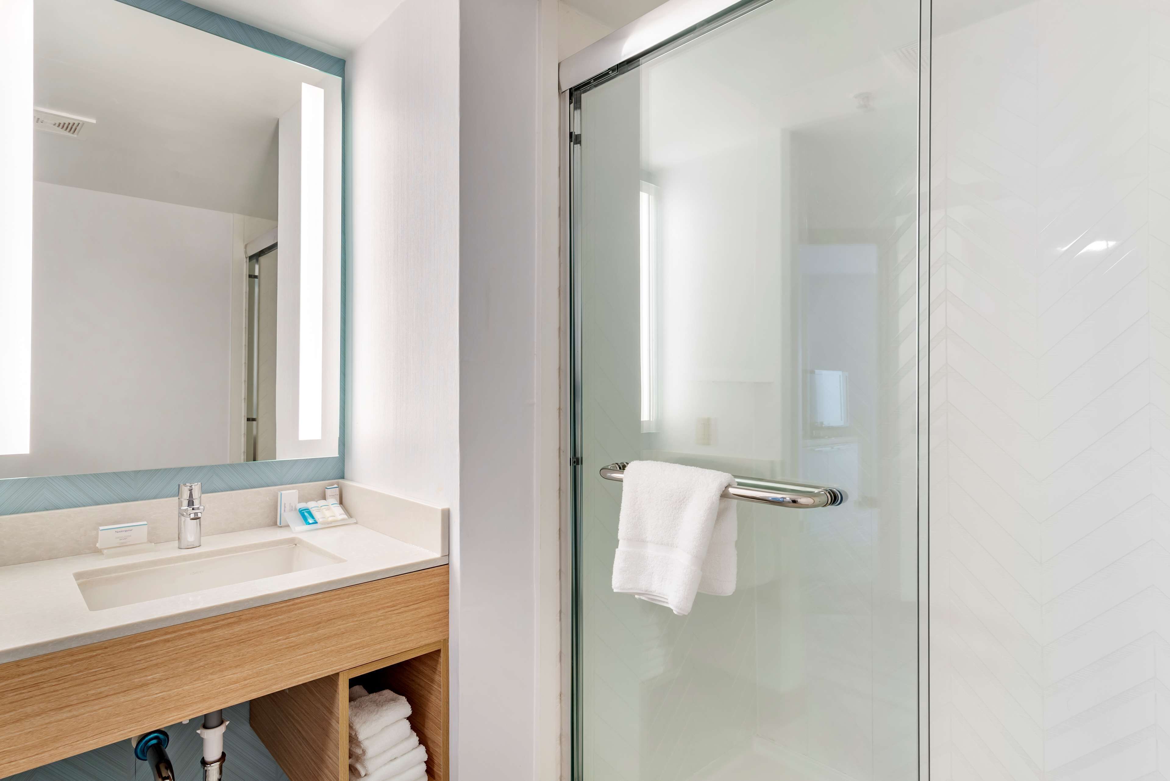 A modern bathroom with a glass shower enclosure, a white sink with a mirror, and a wooden vanity.