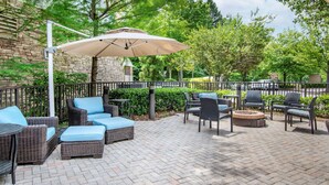 An outdoor patio with wicker furniture, a large umbrella, and a stone wall in the background.