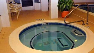 Una pequeña piscina interior con borde azul, una escalera y una planta en maceta cerca.