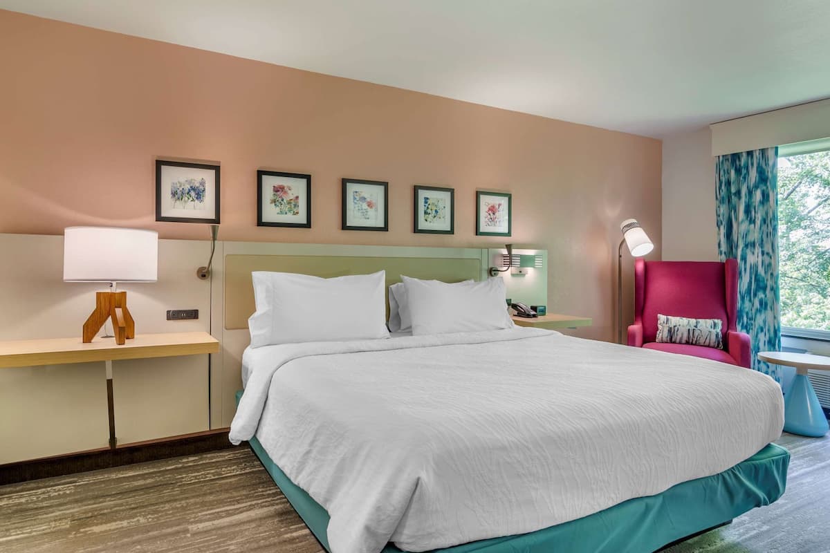 Une chambre d’hôtel avec un grand lit, un bureau avec une lampe, une chaise et des œuvres d’art encadrées accrochées au mur.