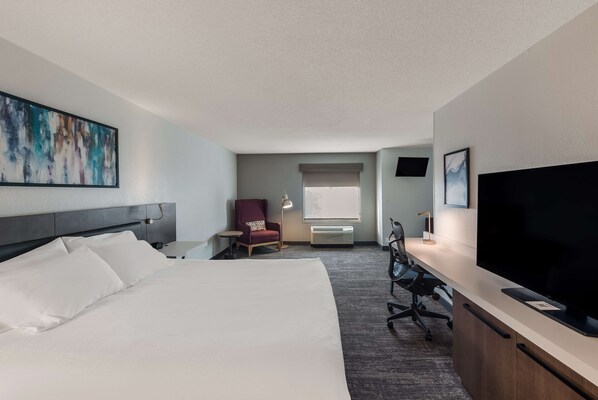A hotel room with a large bed, a desk with a computer, a chair, a TV, and a painting on the wall.